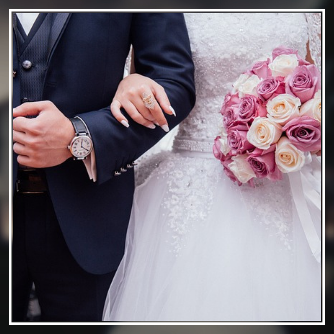 Court marriage Marriage law It depicts a close-up of a bride and groom during a wedding ceremony. The groom is wearing a dark blue suit, while the bride holds a bouquet of pink and cream roses. Their hands are gently clasped, and they exchange rings—a beautiful moment symbolizing commitment and celebration.