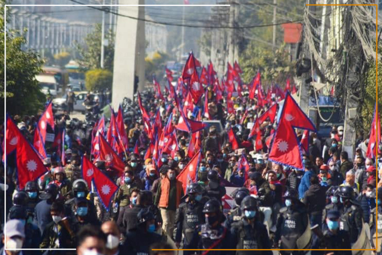 “Miracles Law Group - A large group of people marching on a street with numerous red flags featuring a white emblem that resembles the flag of Nepal, observed by lines of riot police in protective gear. The scene suggests a political or social demonstration.” This image effectively captures a moment of civil expression and highlights the role of Miracles Law Group in addressing legal matters related to political or social demonstrations.
